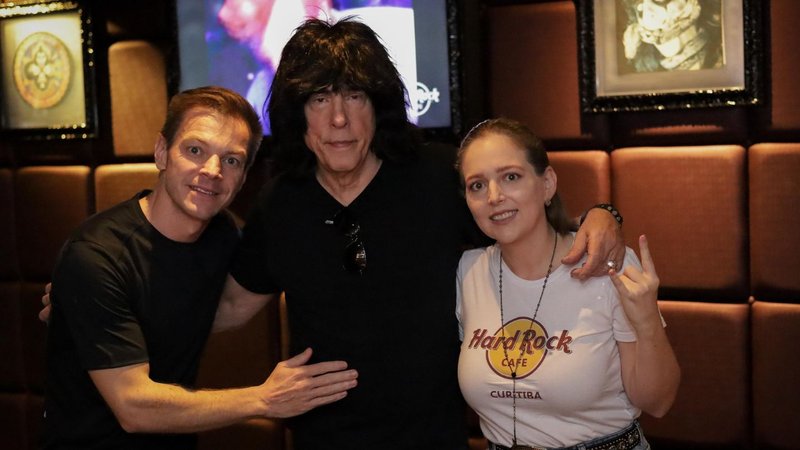 Rafael e Camila Magosso abraçados a Marky Ramone em frente a uma parede estofada