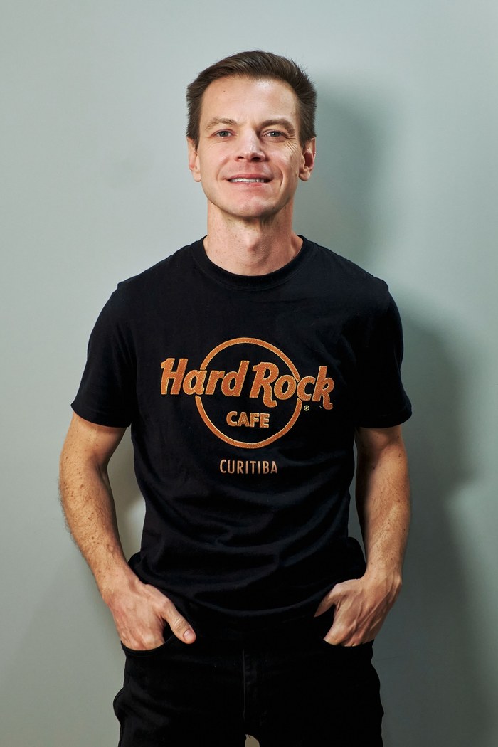 Rafael Magosso sorrindo, de camiseta preta do Hard Rock Cafe Curitiba, mãos nos bolsos